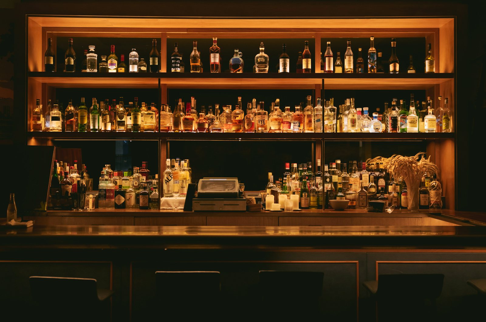 Symmetrisches Flaschenregal hinter einer Bar-Theke, warm beleuchtet vor dunklem Hintergrund